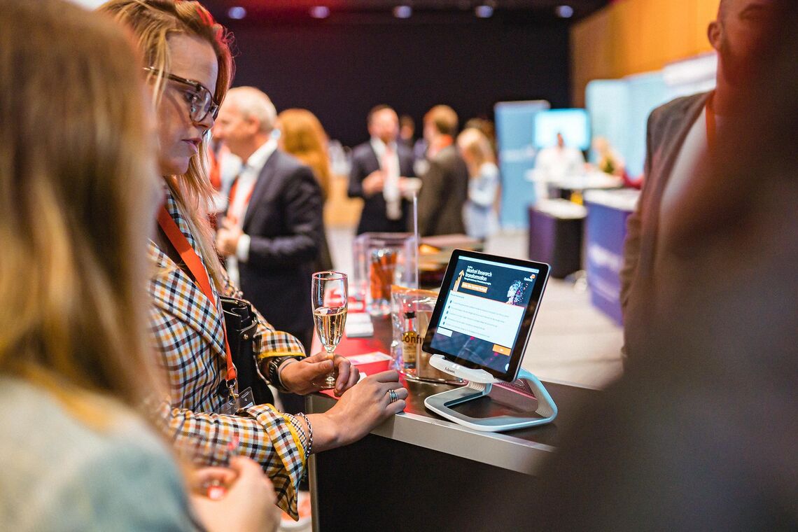 Exhibitor stand attracting attendee interest in front of screen